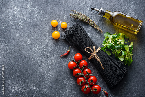 top view of black pasta, tomatoes, olive oil, lettuce, chili peppers on grey background