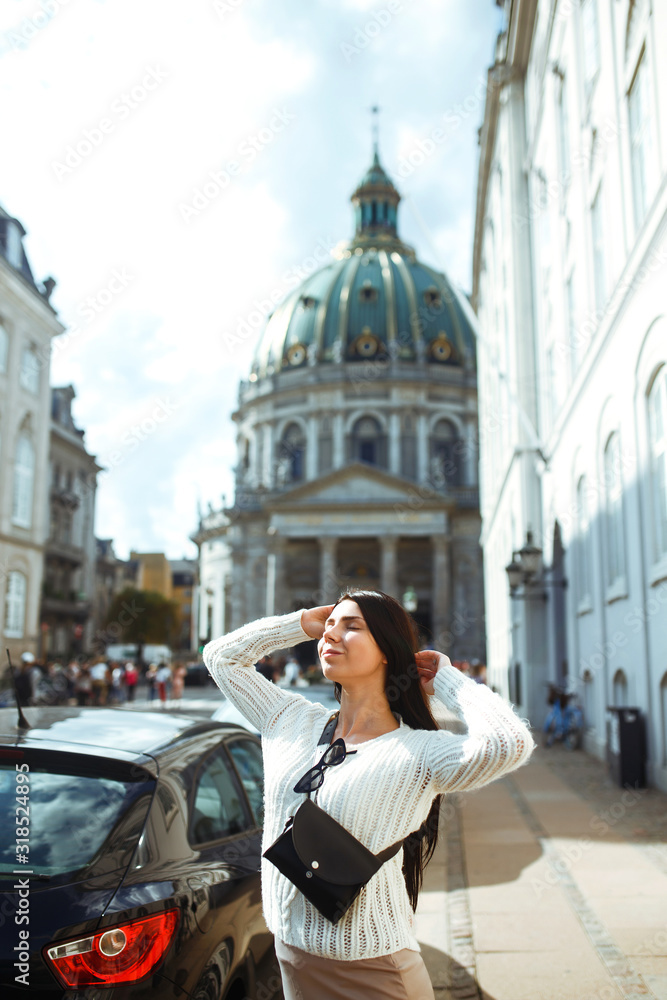 Beautiful stylish girl walks in the city of Norway on a sunny day. Young woman enjoys a stunning scenici sightseeing scandinavian architecture alone. Travelling, lifestyle, adventure, concept.
