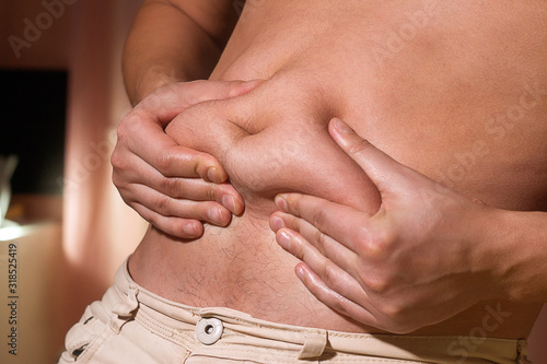 young caucasian man grabbing the fat of his hairy stomach. belly fat, weight loss, overweight photo