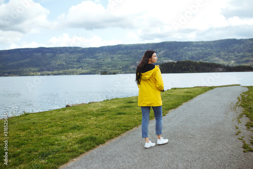 Young woman enjoys freedom against the backdrop of the mountains in the Norway. The girl tourist in a yellow jacket looking on the majestic mountains. Travelling, lifestyle, adventure, concept.