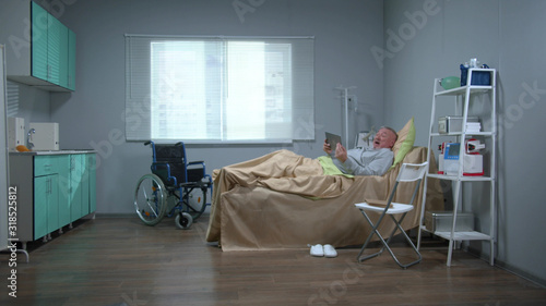 Man lie on the bed in the hospital, watch on tablet and react emotionally  © iaginzburg