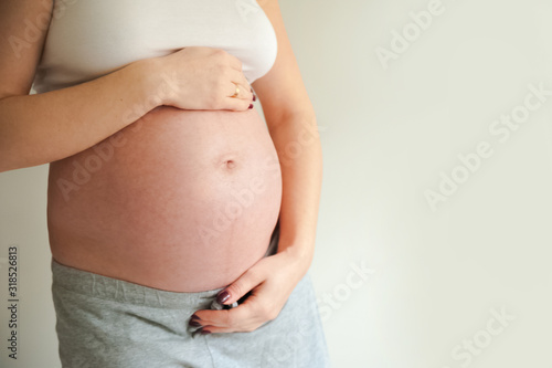 Pregnant cares for her stomach on a gray background close-up and copy space. © Nelly