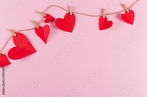 The concept of the preparation for Valentine's Day. Red hearts are held by clothespins on a jute rope, on pink background. Copy space.