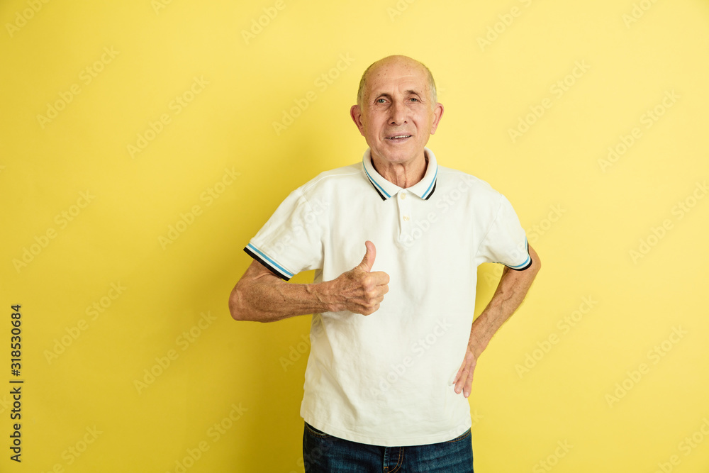 Showing thumb up. Caucasian senior man's portrait isolated on yellow studio background. Beautiful male emotional model. Concept of human emotions, facial expression, sales, wellbeing, ad. Copyspace. Showing thumb up. Caucasian senior man's portrait isolated on yellow studio background. Beautiful male emotional model. Concept of human emotions, facial expression, sales, wellbeing, ad. Copyspace.