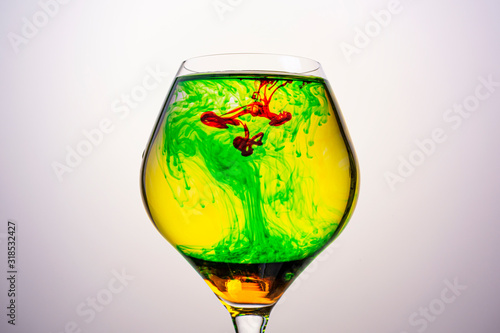 Red , green and yellow food coloring diffuse in water inside glass , with gradient background