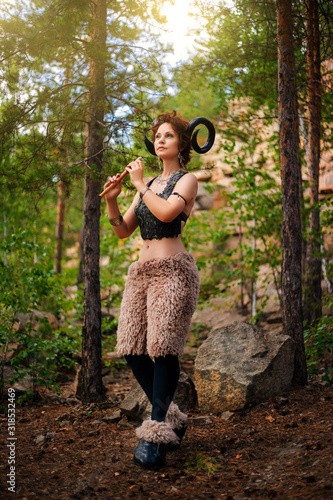 Foto A girl in the image of a faun stands with a wooden flute
