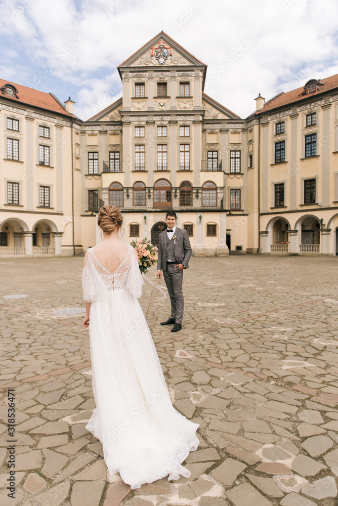 Obraz premium Beautiful elegant couple of newlyweds in love on the background of an old building and paving stones, European wedding
