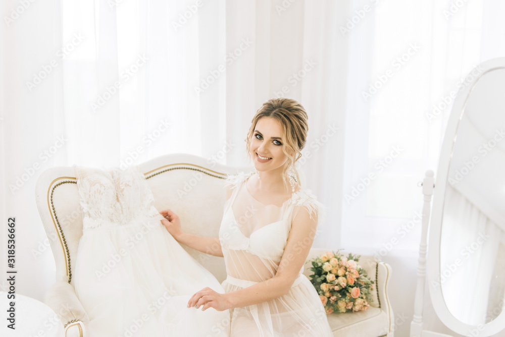 Portrait of a beautiful young bride in a bright room in a romantic atmosphere. Bride in a negligee with a wedding dress Portrait of a beautiful young bride in a bright room in a romantic atmosphere. Bride in a negligee with a wedding dress