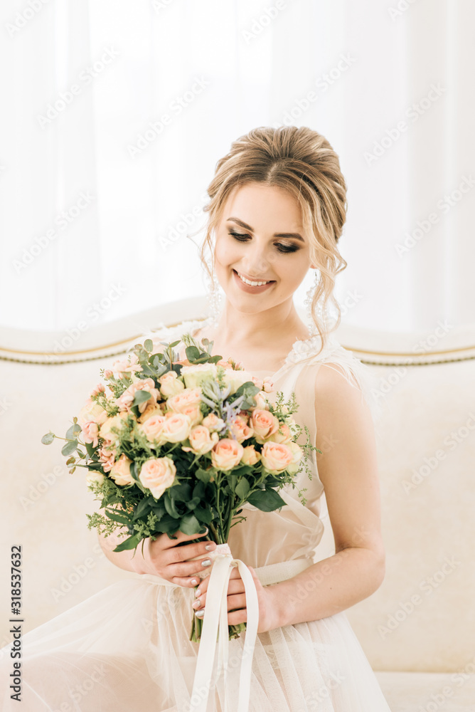 Portrait of a beautiful young bride in a bright room in a romantic atmosphere. Bride in a negligee with a wedding bouquet