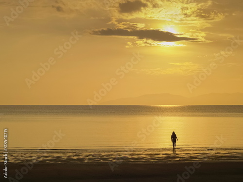 view seaside evening of a woman standing on sand beach with yellow sun light and cloudy sky background, sunset at Pak Meng Beach, Trang Province, southern of Thailand. © Yuttana Joe