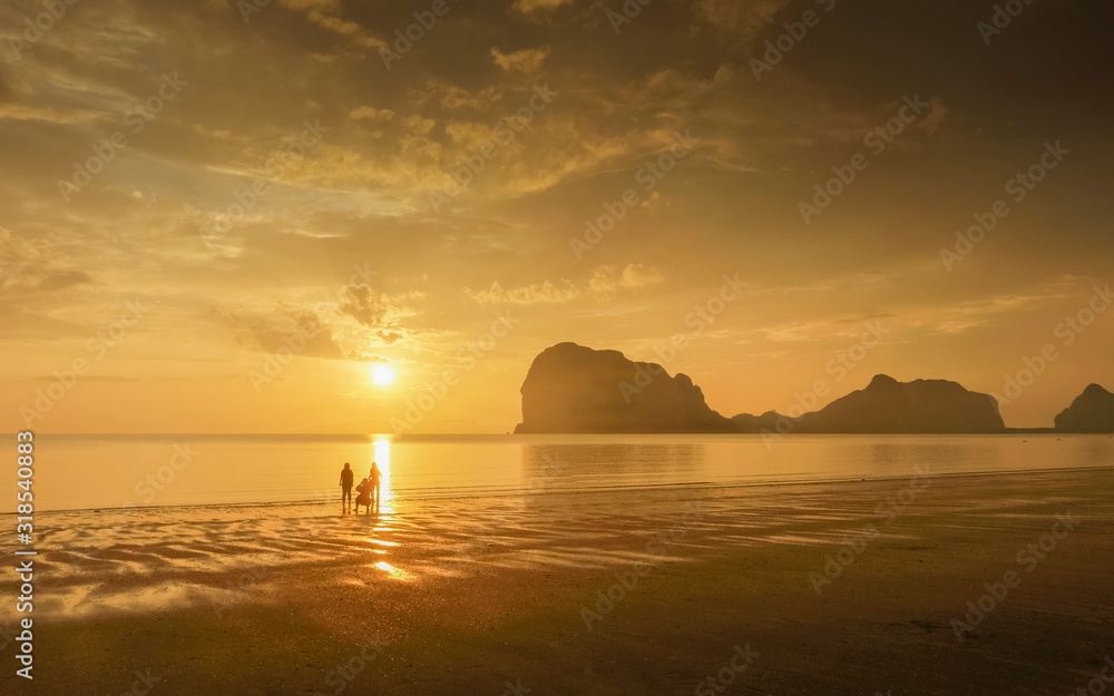 view seaside evening of tourists walking relax on sand beach with mountain and yellow sun light and cloudy sky background, sunset at Pak Meng Beach, Trang Province, southern of Thailand.