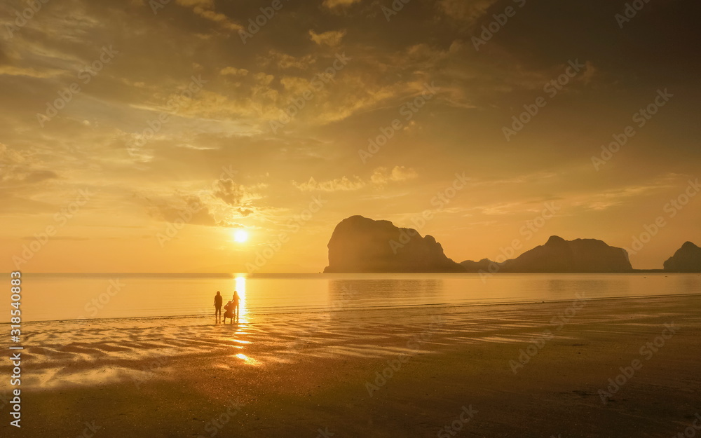 view seaside evening of tourists walking relax on sand beach with mountain and yellow sun light and cloudy sky background, sunset at Pak Meng Beach, Trang Province, southern of Thailand. view seaside evening of tourists walking relax on sand beach with mountain and yellow sun light and cloudy sky background, sunset at Pak Meng Beach, Trang Province, southern of Thailand.