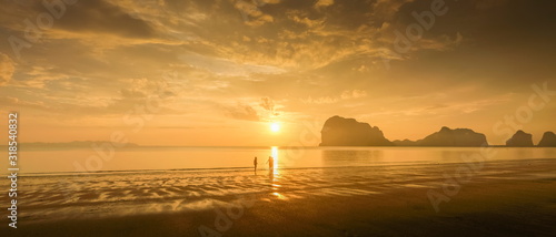 view seaside evening of tourists walking relax on sand beach with mountain and yellow sun light and cloudy sky background  sunset at Pak Meng Beach  Trang Province  southern of Thailand.