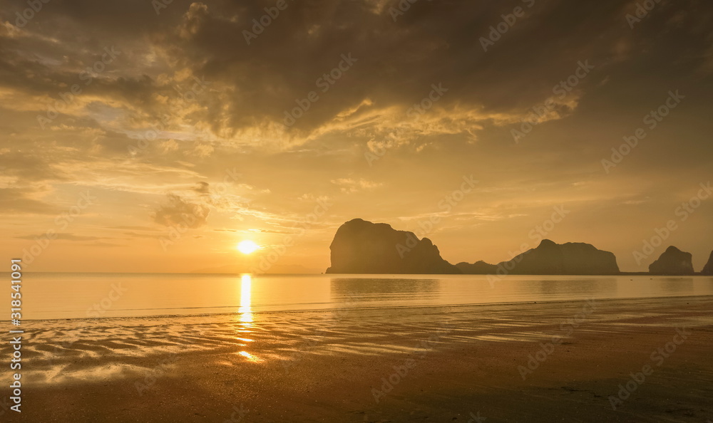 view seaside panorama evening of mountains on the beach with reflection on woater and yellow sun light with cloudy sky background, sunset with raining at Pak Meng Beach, Trang Province, Thailand.