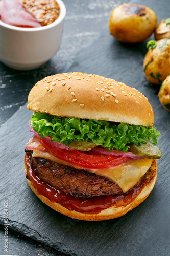 Delicious cheeseburger with baked potatoes and broccoli on a black stone board served with a glass of lager beer.