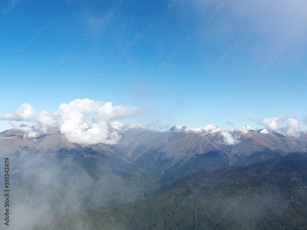 View of a mountain valley with snowy peaks in a light cloudy haze View of a mountain valley with snowy peaks in a light cloudy haze