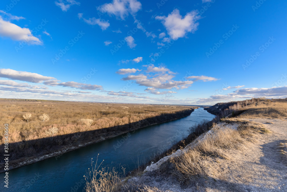 panorama of nature in early spring. river in the sun, cloudy blue sky at sunset