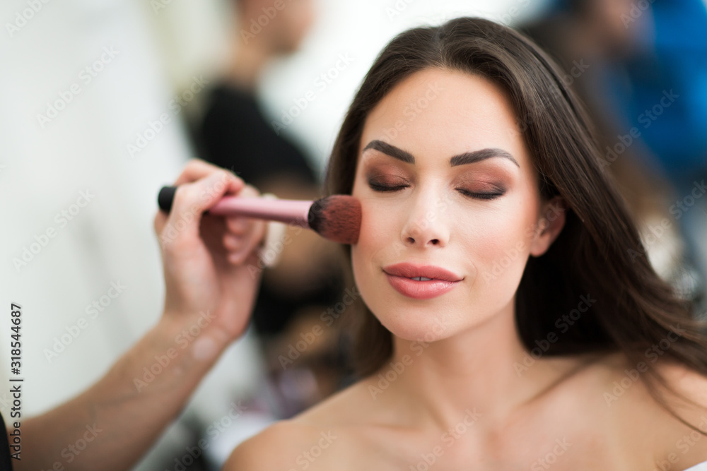 Makeup artist preparing beautiful female model for shooting