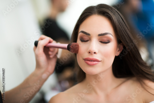 Makeup artist preparing beautiful female model for shooting