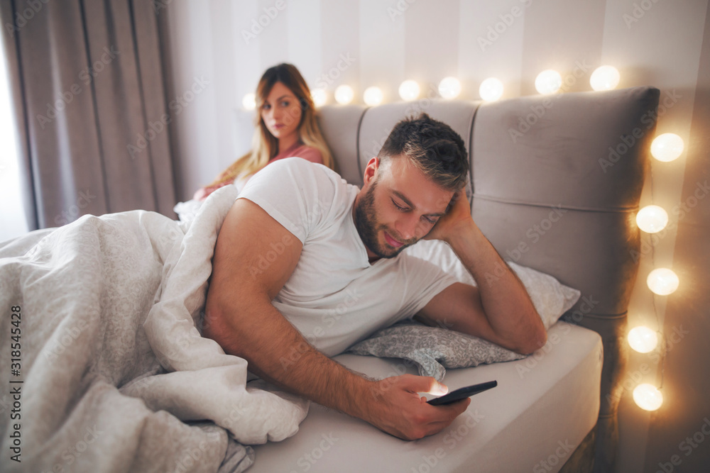Tableau sur toile Couple lie in bed and man using phone.