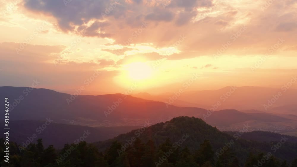 Lens flare of sun through tops of fir trees on panorama of mountain landscape at sunset and bright disk of sun in morning in summer against blue sky aerial view of drone up. Nature. Travel Lens flare of sun through tops of fir trees on panorama of mountain landscape at sunset and bright disk of sun in morning in summer against blue sky aerial view of drone up. Nature. Travel
