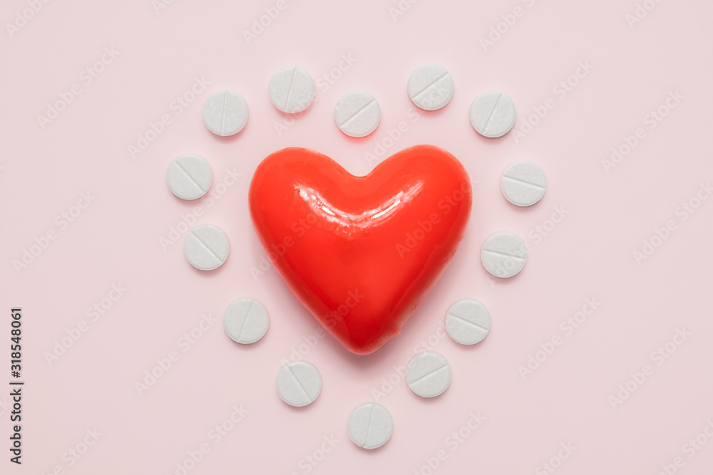 Heart and pills in the shape of a heart on pink background, top view. Cardiology, heart disease concept. Heart and pills in the shape of a heart on pink background, top view. Cardiology, heart disease concept.