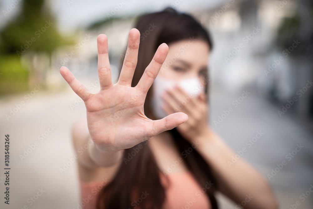 Woman feeling sick, coughing or sneezing. holds the hand in front of her, sign to stop. She wearing protective mask.