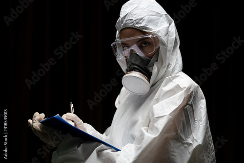 Woman wearing gloves with biohazard chemical protective suit and mask. is writing report on paper.