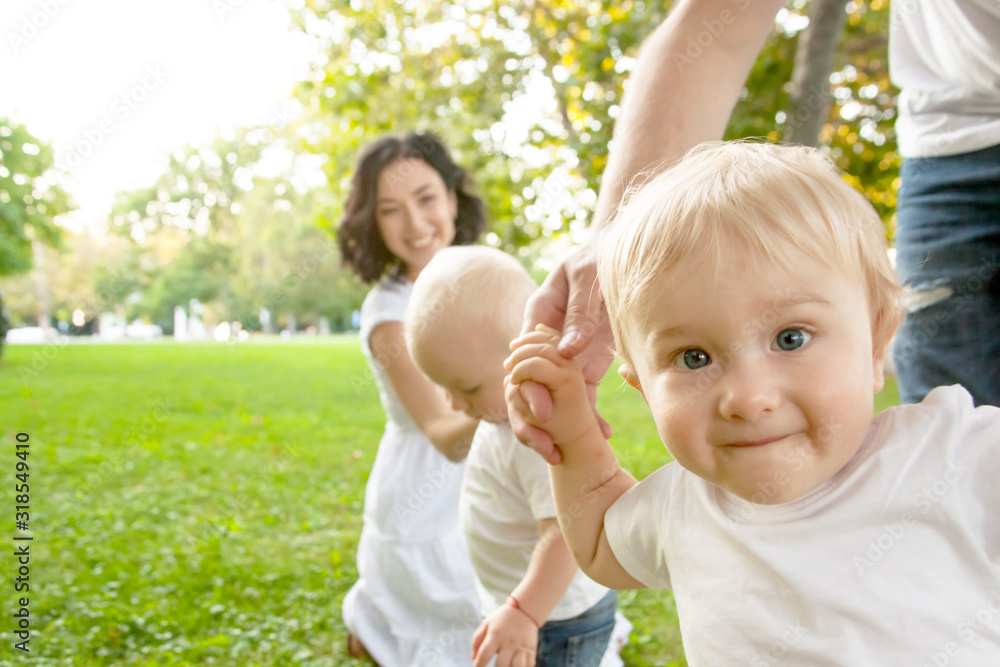 Happy family resting on the park with green grass. Father study the kid walking . Small twins are hape to spend time with parent. Happy family resting on the park with green grass. Father study the kid walking . Small twins are hape to spend time with parent.
