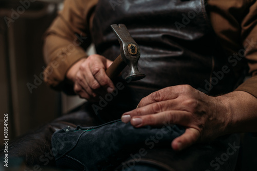 Cropped view of shoemaker holding hummer while repairing shoe in workshop