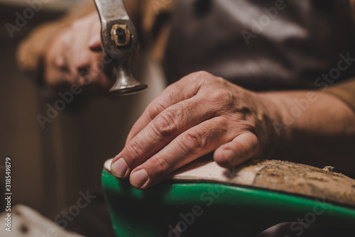 Fotografie cropped view of shoemaker holding hummer while repairing shoe in workshop