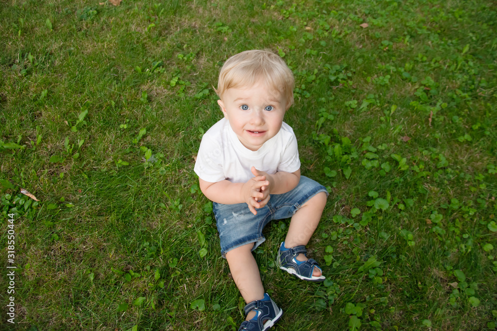 Alone baby sit on the green gras on the park. the kid wearing jeans and white t-shirt Alone baby sit on the green gras on the park. the kid wearing jeans and white t-shirt