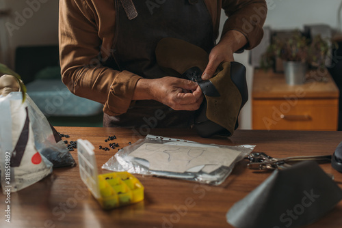 cropped view of cobbler holding piece of leather near desk with tools photo