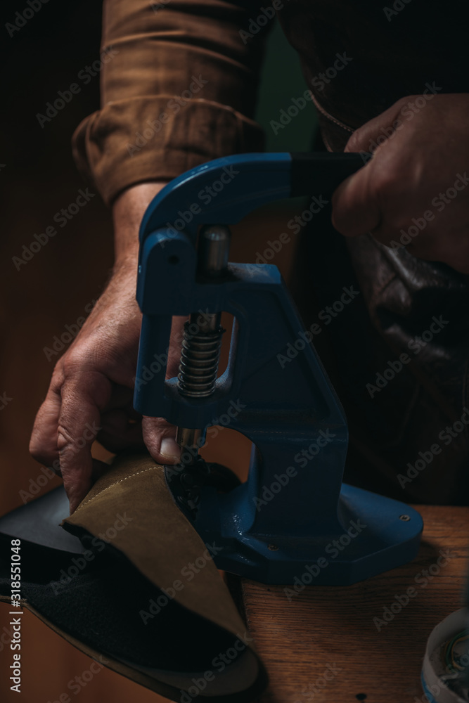 Obraz premium cropped view of shoemaker making holes in leather with puncher