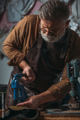 senior shoemaker making holes in leather with puncher