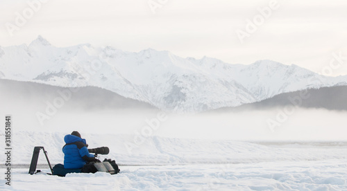 Silhouette of photographer on the snow with tripod and camera . Winter morning fog.