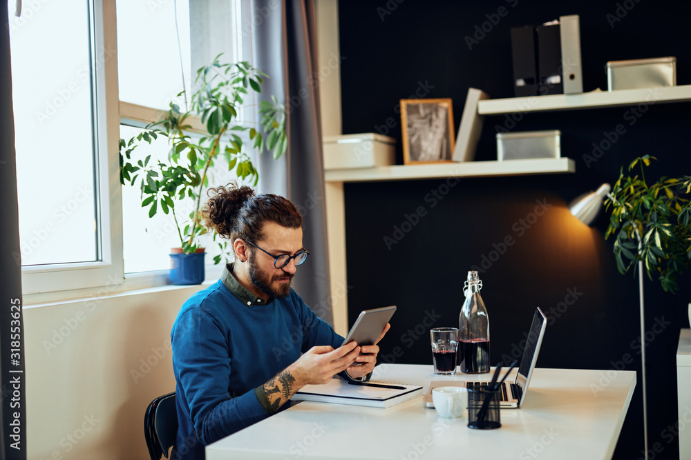 Young attractive caucasian bearded graphic designer sitting at office and using tablet. Young attractive caucasian bearded graphic designer sitting at office and using tablet.