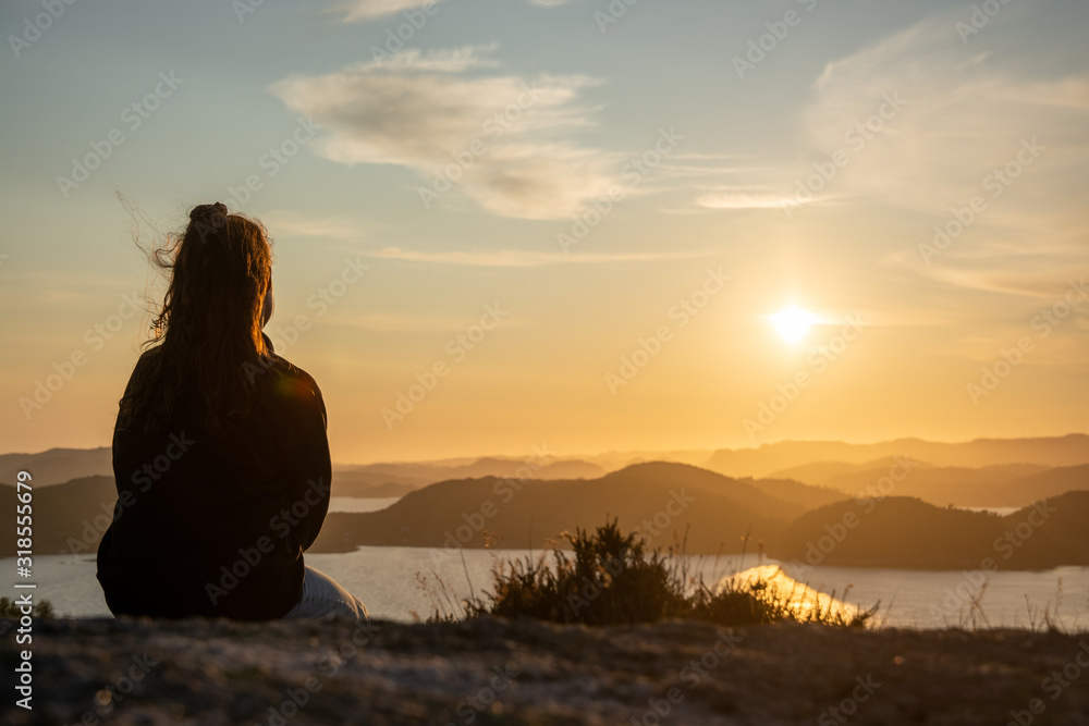 unknown woman on top of a rocky mountain overlooking the sea. Sunset is warming the sky. High dynamic range