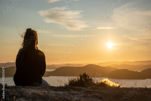 unknown woman on top of a rocky mountain overlooking the sea. Sunset is warming the sky. High dynamic range
