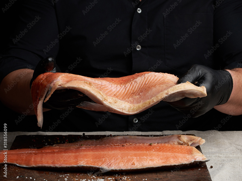 Obraz premium chef in a black shirt and black latex gloves holds a large piece of salmon fish fillet