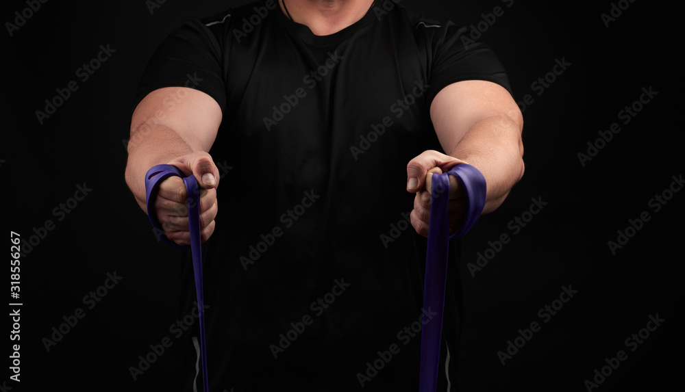 athlete with a muscular body in black clothes is doing physical exercises with purple rubber