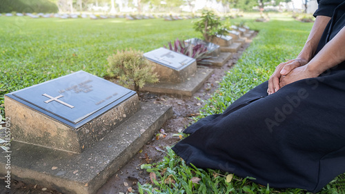Принти на полотні Mourning young woman kneeling at her family grave in beautiful green cemetery