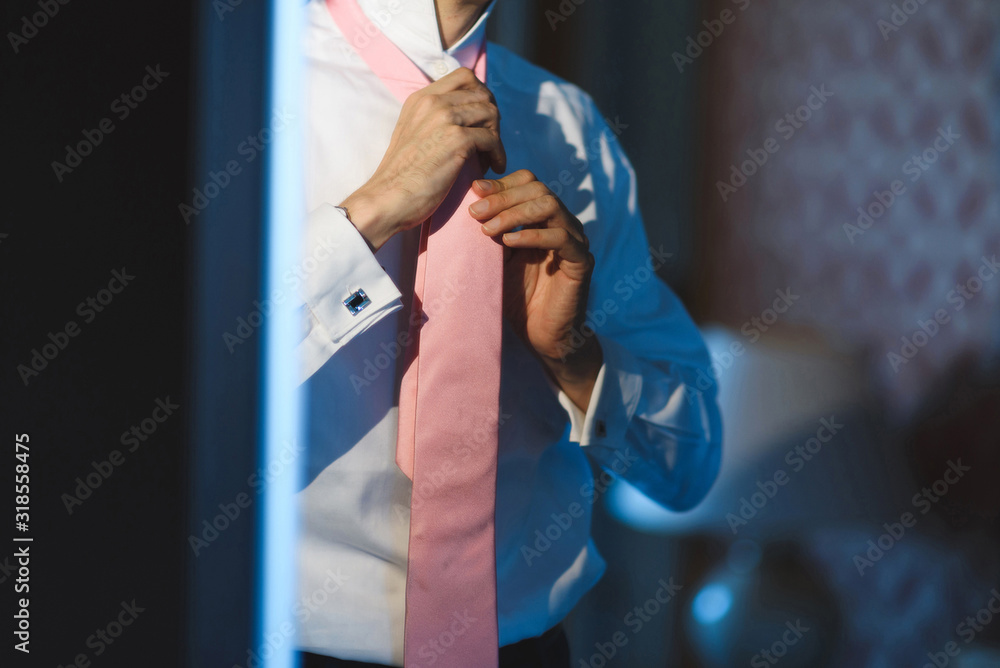 man knotting pink tie at mirror