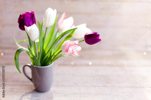 Fototapeta Naklejka Na Ścianę i Meble -  Tulips at wooden background. Spring flowers in gray cup. Bouquet in vase. Pink, white, lilac and purple blooming flora in sunshine. Cozy still life. Copy space.