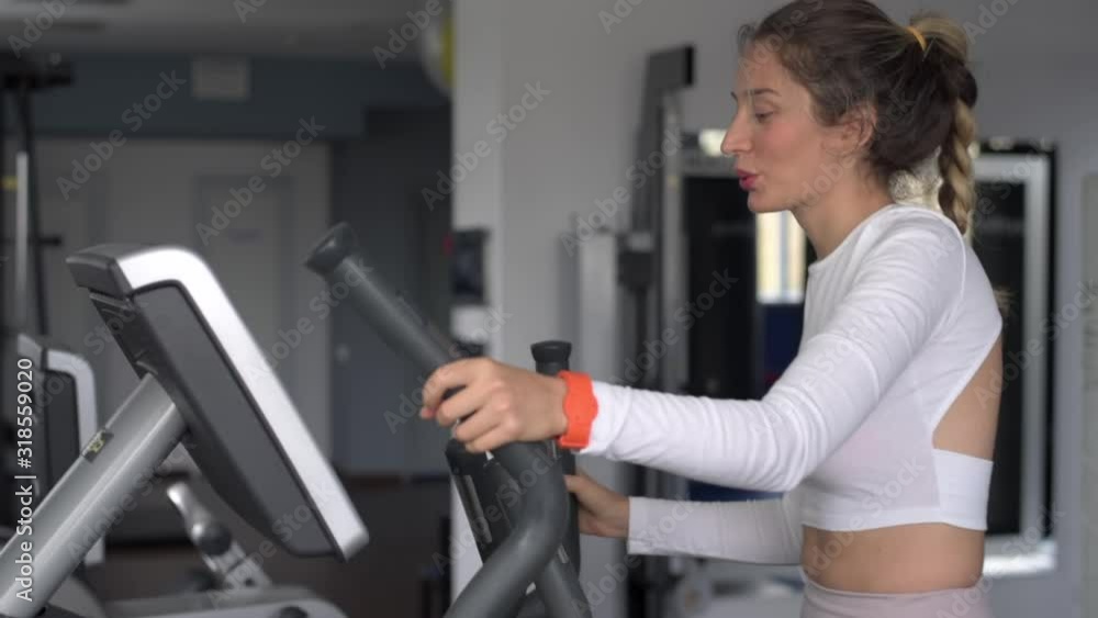 Woman in white sport suite running on fitness machine at the club Woman in white sport suite running on fitness machine at the club