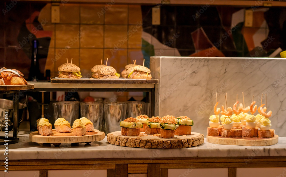 Obraz premium Traditional spanish snacks, appetizers or tapas called pintxos in a bar or cafe in San Sebastian, Basque country, Spain. A bar counter in a typical restaurant or tapas bar.