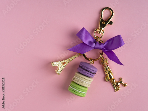 Elegant accessory key chain with golden eiffel tower and colorful macarons on pink background, place for text, copy space. Present gift, fashion pendant.