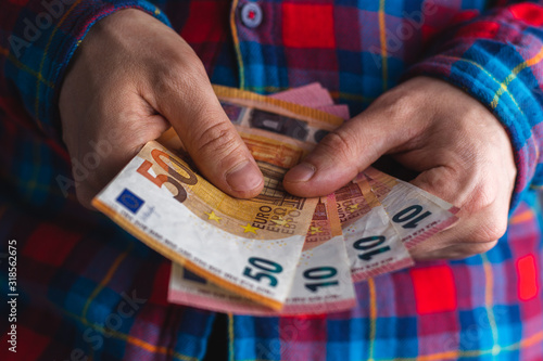 man in a red and blue plaid shirt counts money in hands. Man hands holding pile of money. pile of 10 and 50 euro banknotes in man hands