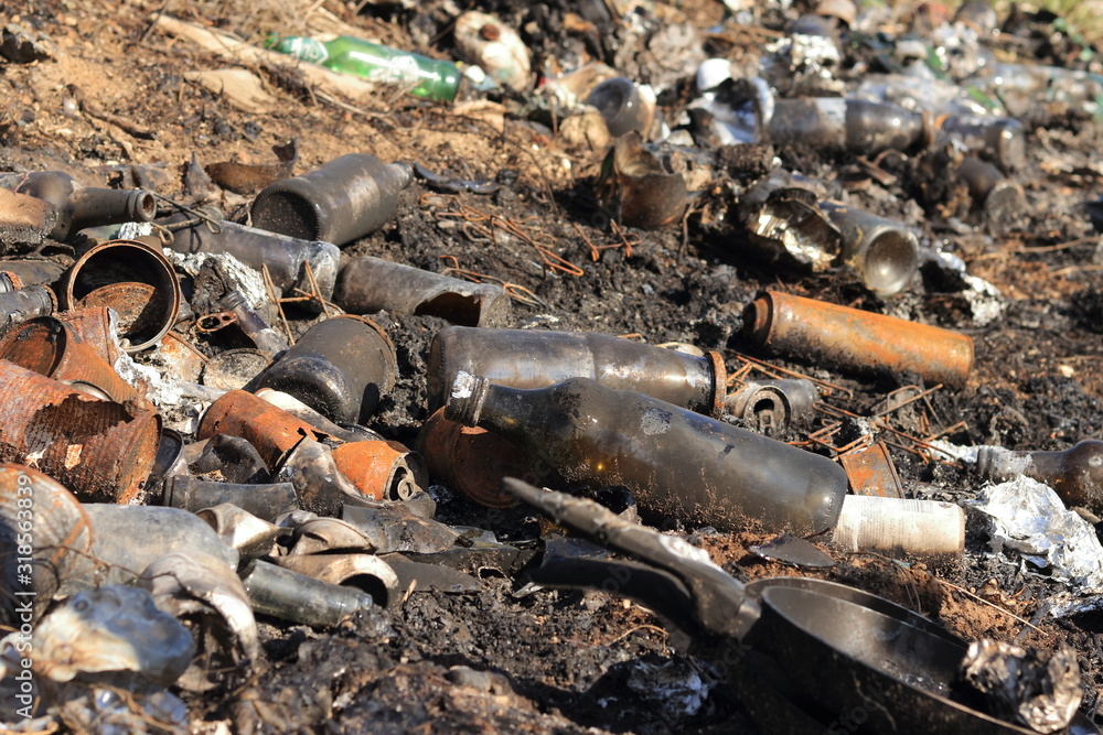 Fototapeta premium Dump with mound of waste (rubbish) on ground. A lot of litter and trash from bottles, cans, glass, metal, plastic and other refuse. Heap of garbage have been burn in fire.