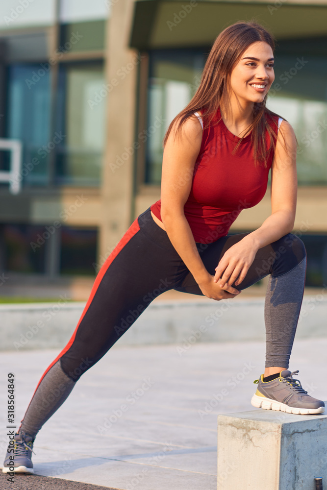 Fototapeta premium Young woman exercising / stretching in urban park.